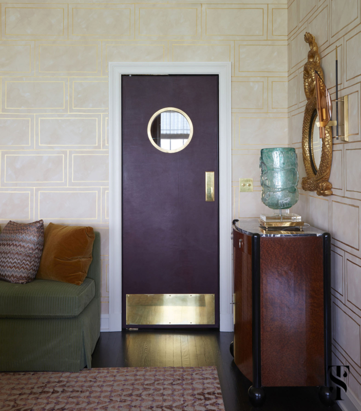 The dining room of a Chicago co-op designed by Summer Thornton featuring a custom designed hand painted wallcovering with gold rectangles & a port hole style butler's door.