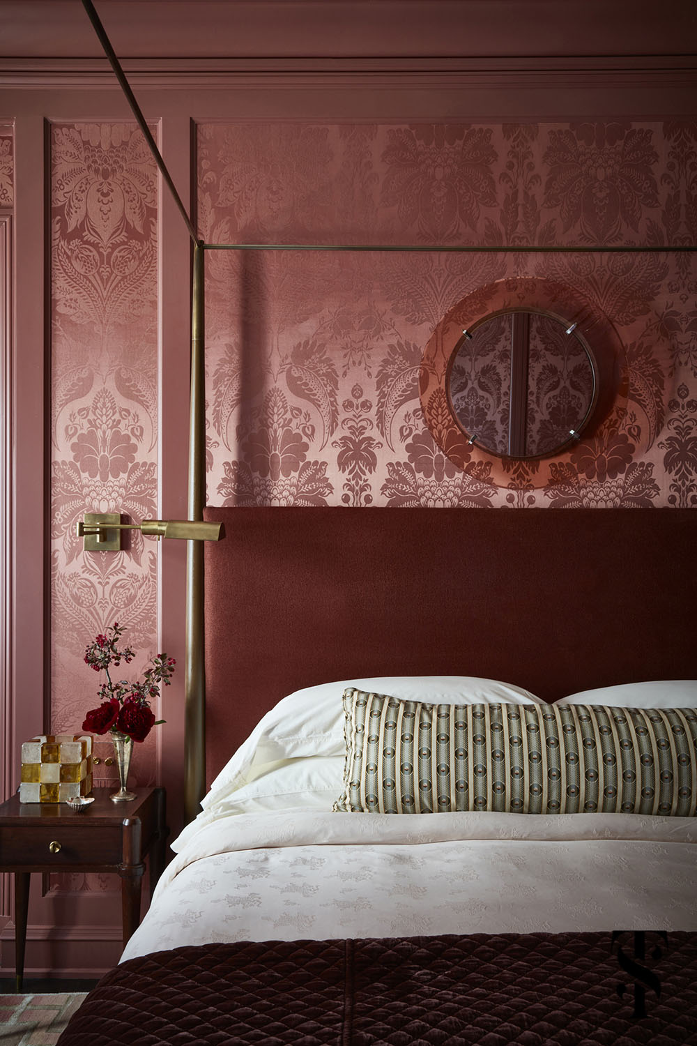 A sultry master bedroom featuring de Gournay pineapple demask in raspberry, a walnut bed from Dennis Miller Associates, swing arm sconces by Circa Lighting, and an Italian Fontana Arte Mirror.