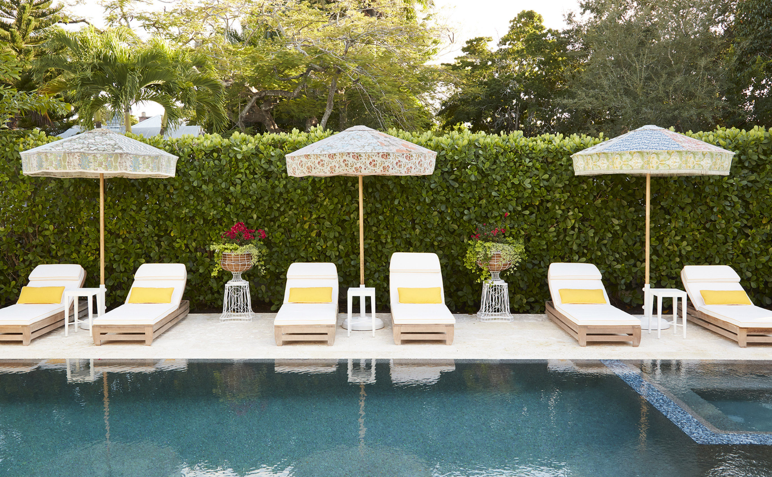 Playful umbrellas & a hedge wall surround a pool with interior design by Summer Thornton for a home in Naples Florida.